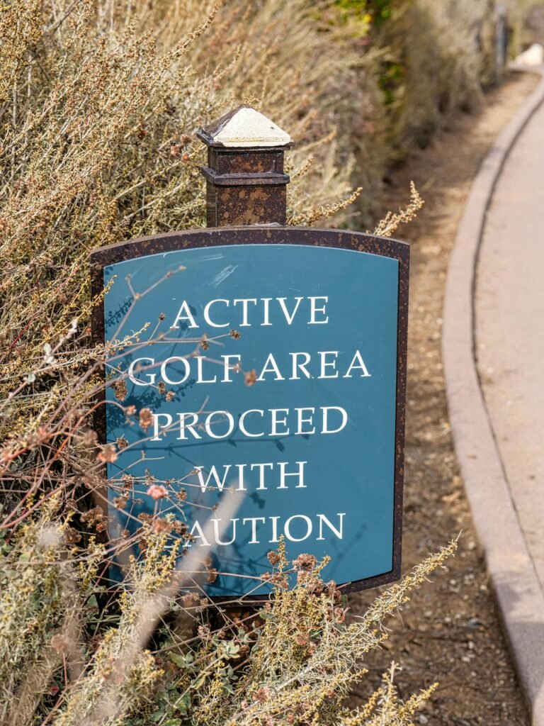 Sign in a golf park warns to proceed with caution, surrounded by foliage.